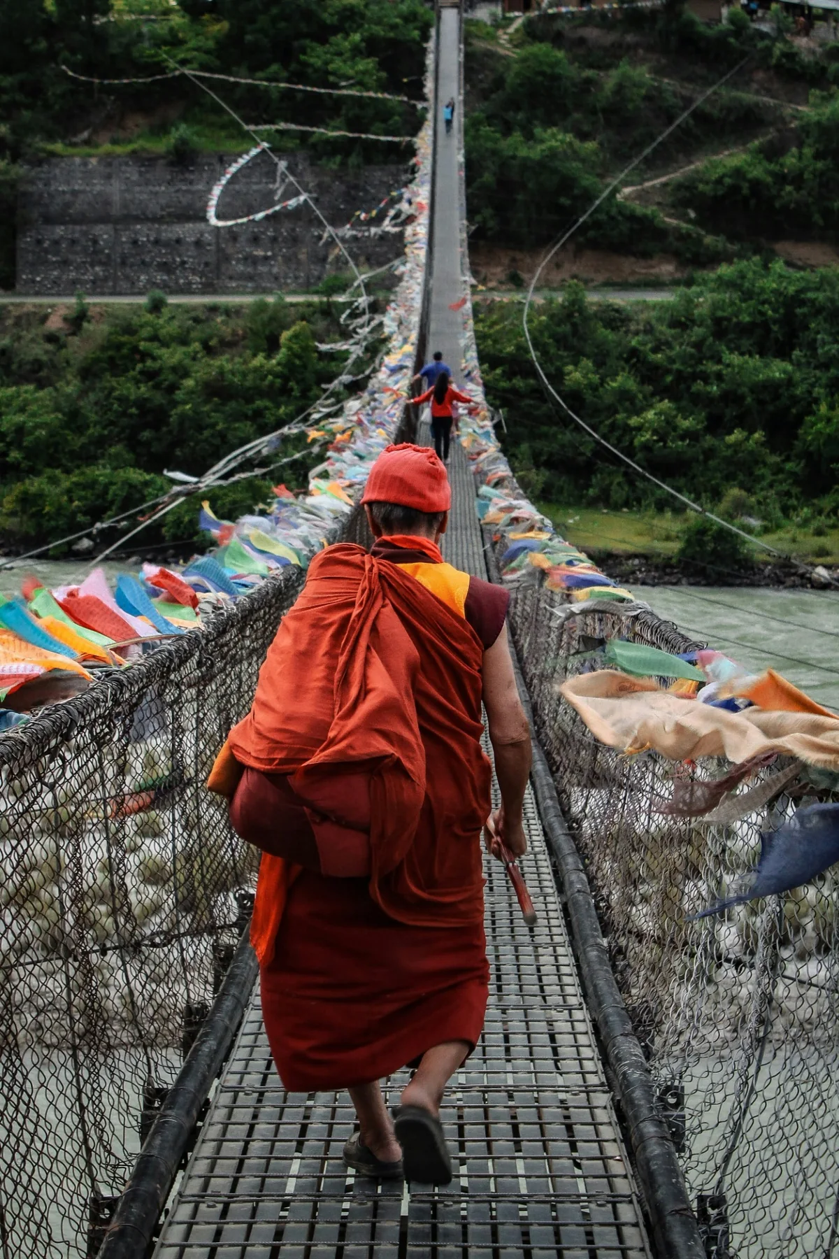 A Buddhist monk crossing a prayer-flag-covered suspension bridge in Bhutan