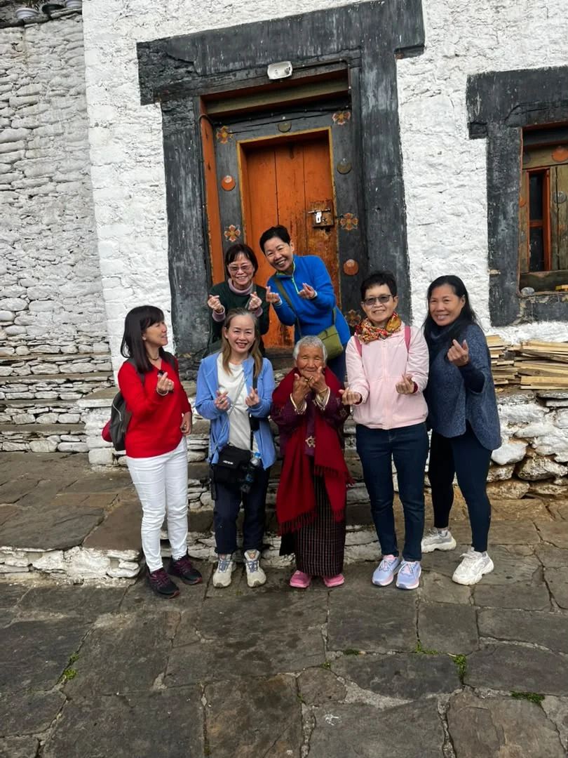 Travellers sharing a joyful moment with a Bhutanese elder outside a traditional home